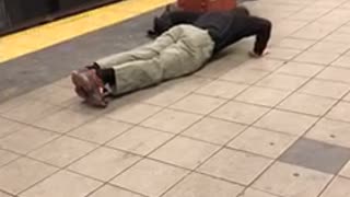 Guy does push ups on the floor of a subway station