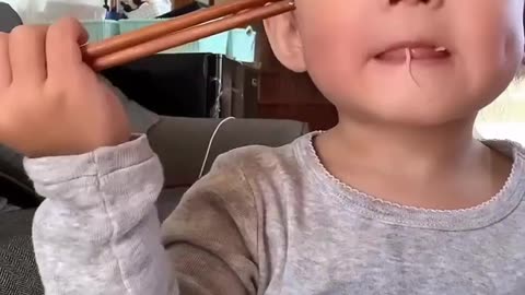 1 year old baby eating fried noodles with chopsticks