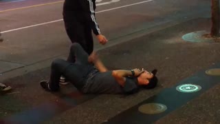 Guy in grey shirt falls from skateboard, lies on ground smoking