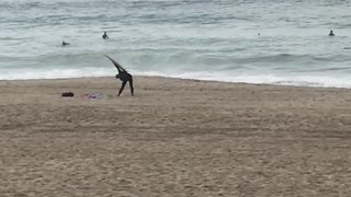 Guy uses surfboard to stretch on the beach