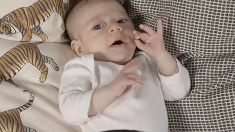 Baby yawning while lying face-to-face on a bed.