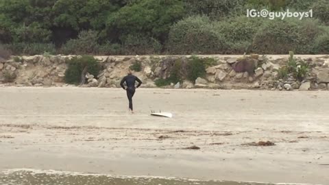 Surfer walking on beach with surfboard tied to leg following him
