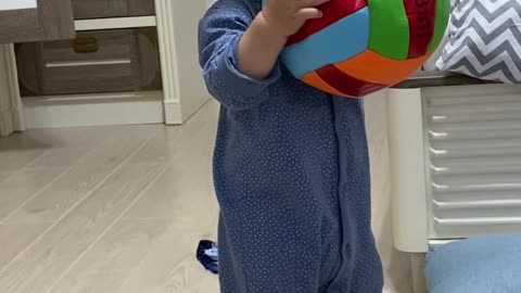 Cute baby try to learn how to play basketball at home under mom coaching