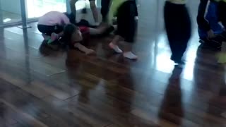 Little girls holding onto each others neon green shirts one girl in red falls and hits floor