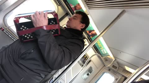 Man plays accordion with his eyes closed on subway
