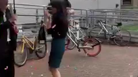 Girl holding champagne bottle gets startled by cork that hits umbrella