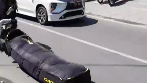 Guy dragging black bag on floor ground street while riding motorcycle with helmet