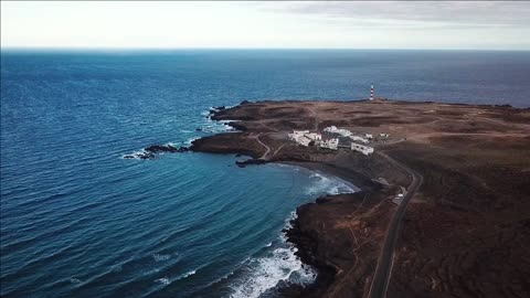 view from the height of rocky coastline with white buildings and a lighthouse on tenerife canary