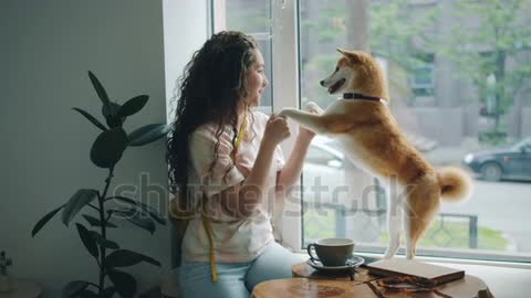 Happy young woman is dancing with pet dog sitting on window