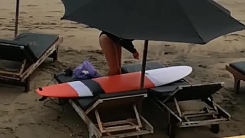 Music girl waxing orange surfboard under black umbrella