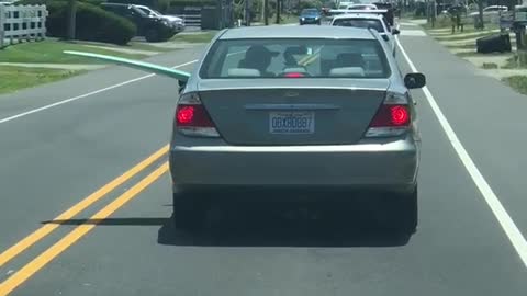 Silver car driving with blue surfboard out of driver rear passenger window