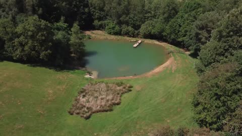 Drone Shot Flying Through Brick Arch to Reveal a Scenic Lake On Edge of Woodland